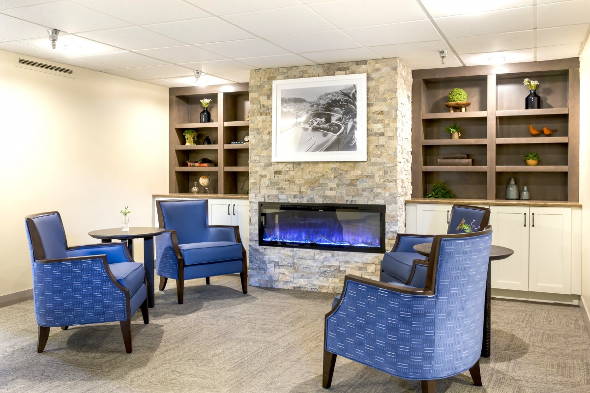 A modern living room featuring blue chairs, a stylish fireplace, and built-in bookshelves.