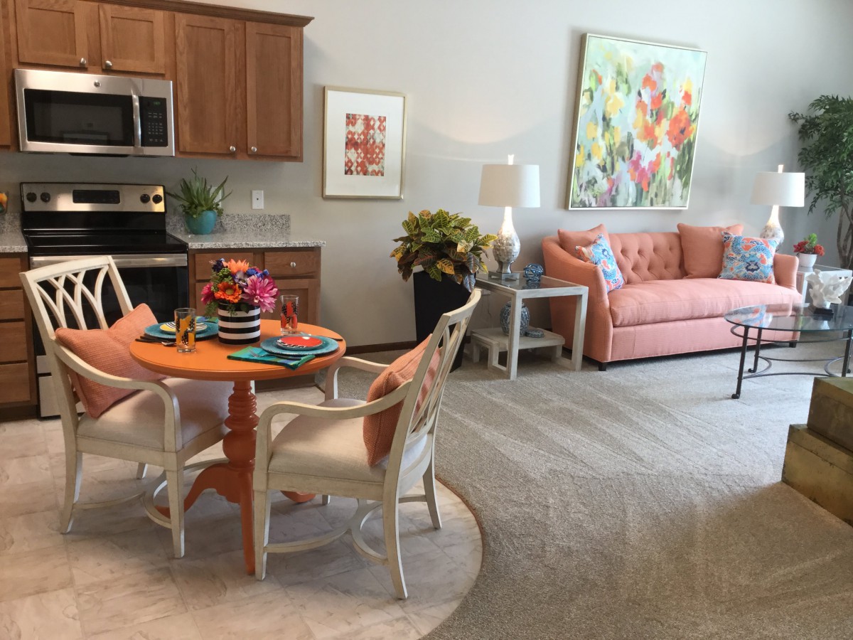 A cozy living and dining space with an orange sofa, vibrant artwork, and a compact kitchen area.