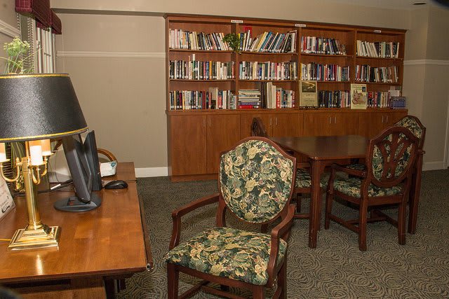 A cozy library with bookshelves, chairs, and a desk equipped with a computer.