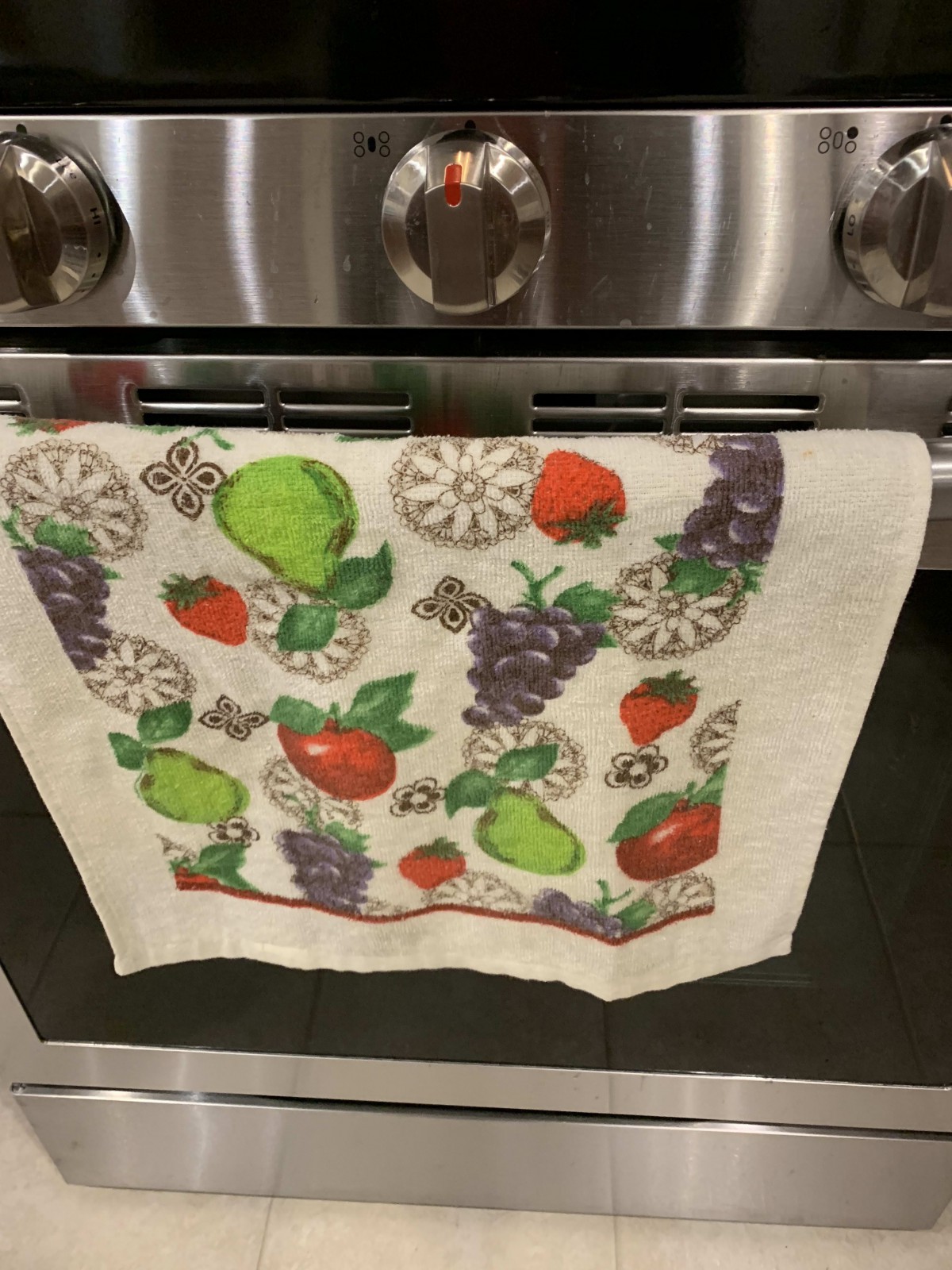 A colorful kitchen towel with fruit designs hanging on an oven handle.