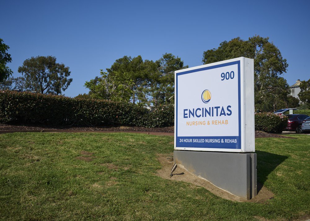 A sign at the entrance of the Encinitas building against a backdrop of trees and clear blue sky.