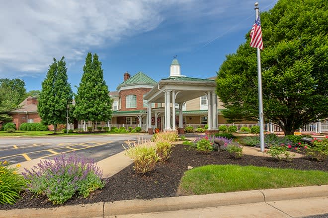 A well-maintained building entrance with landscaping and an American flag on a clear day.