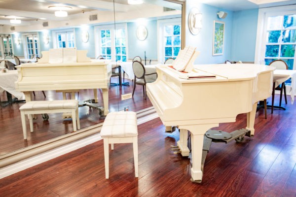 A bright music room with a white grand piano and mirrored walls.