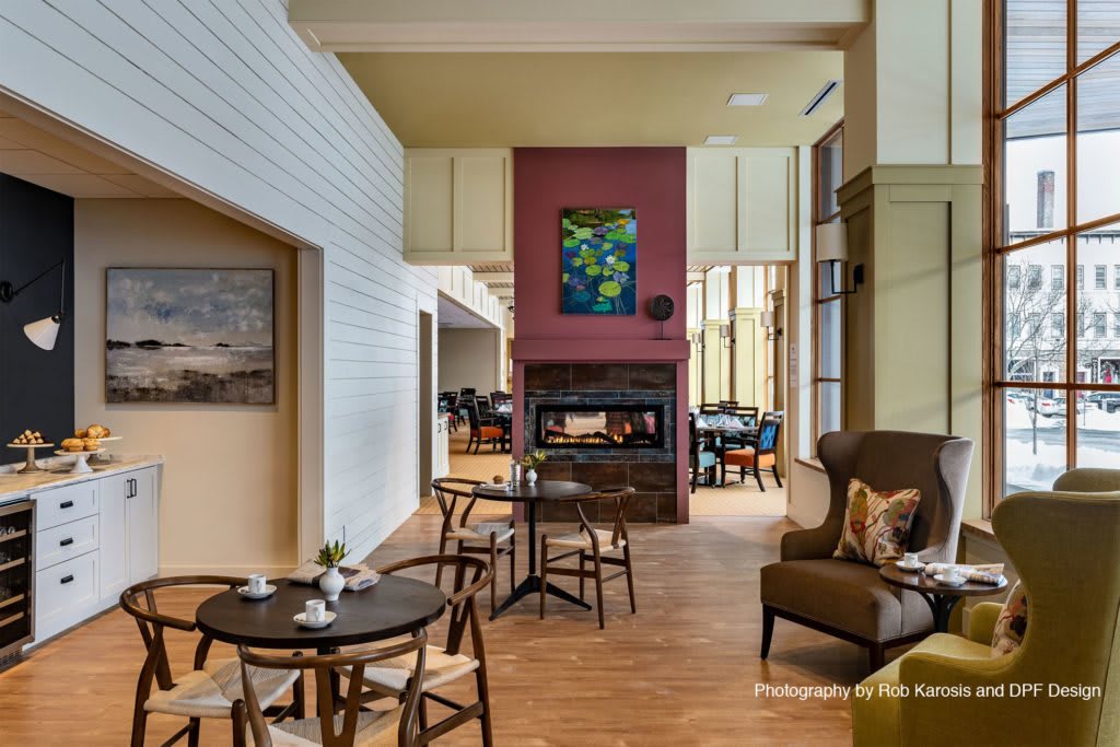 A cozy lounge area with a fireplace, tables, and chairs, decorated with colorful art.