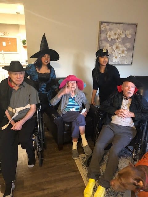 A group of people dressed in Halloween costumes, wearing various hats, posing for a photo indoors.