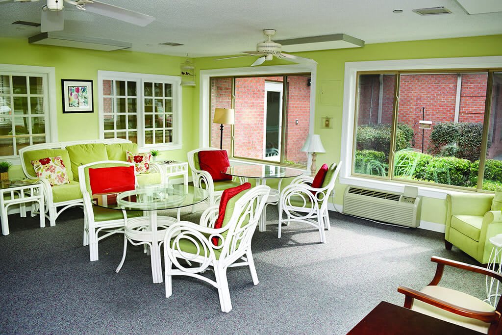 A bright sunroom with wicker furniture, glass tables, and large windows.