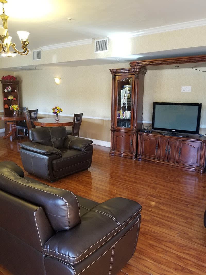 A spacious living room featuring leather seating, a large television, and a wooden dining set on polished hardwood floors.