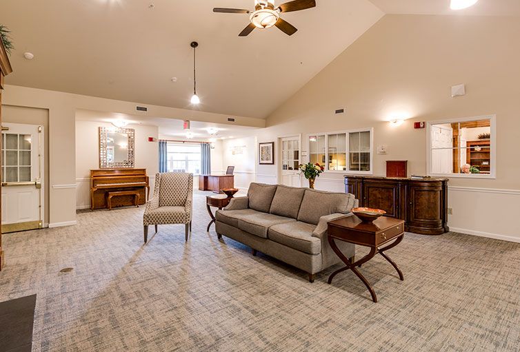 A spacious living room with a sofa, chair, and piano under a ceiling fan.