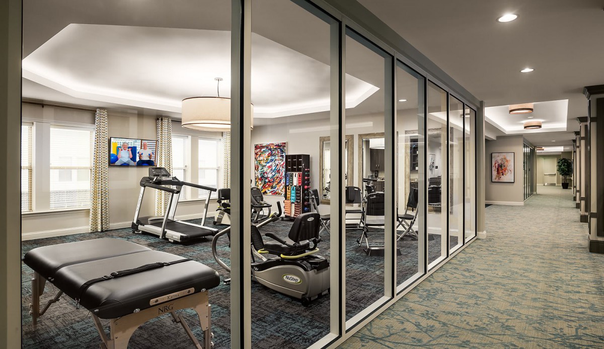 A modern gym with various exercise equipment, featuring glass walls and a sleek design.