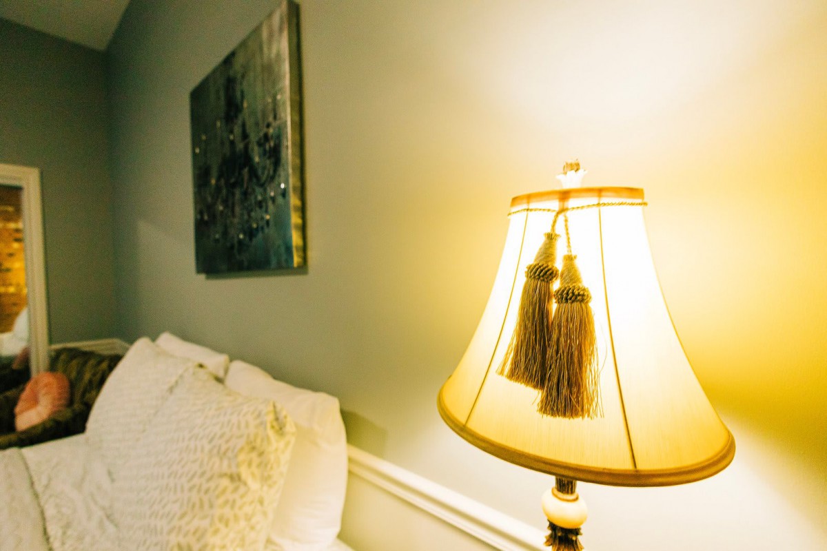 A cozy bedroom corner with a warmly lit lamp and soft bedding.