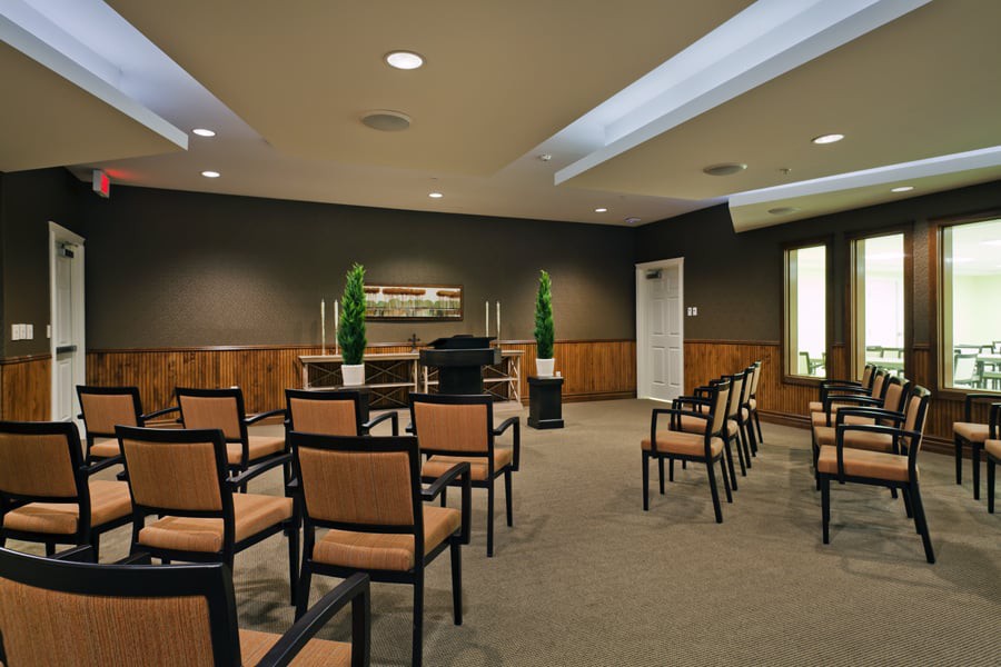 This image shows a neatly arranged conference or meeting room with rows of chairs, potted plants, and a carpeted floor.