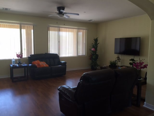 A cozy living room with sofas, a wall-mounted television, and large windows.