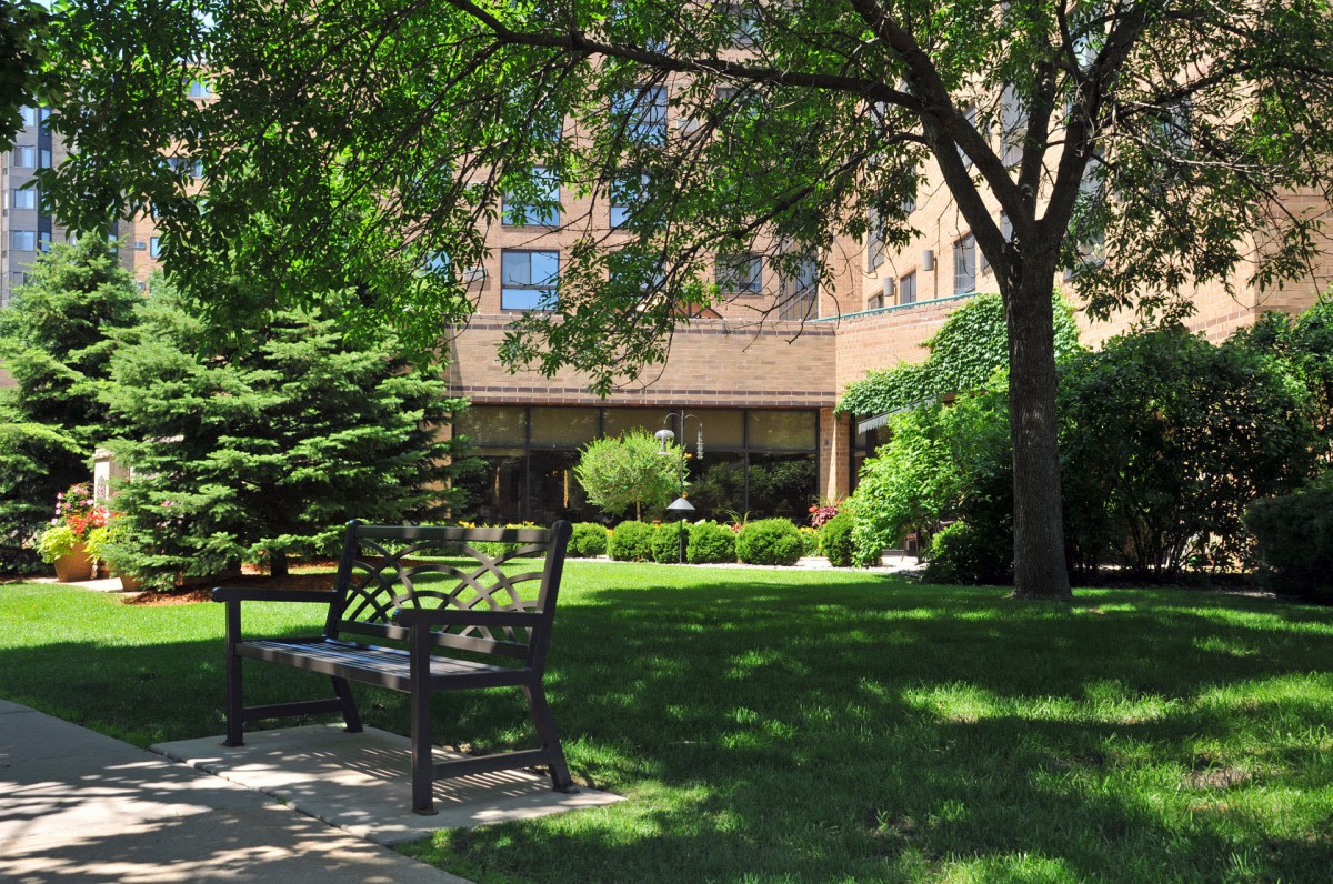 A peaceful garden area with benches and lush greenery in front of a building.