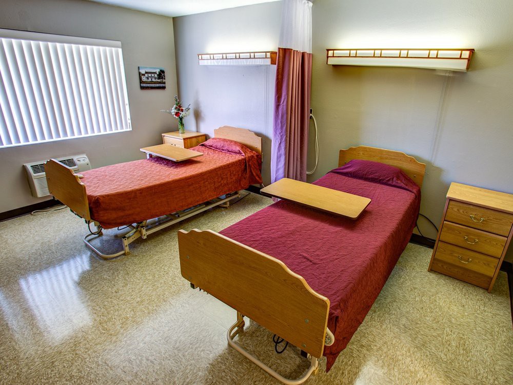 A hospital room with two beds, side tables, and a privacy curtain.