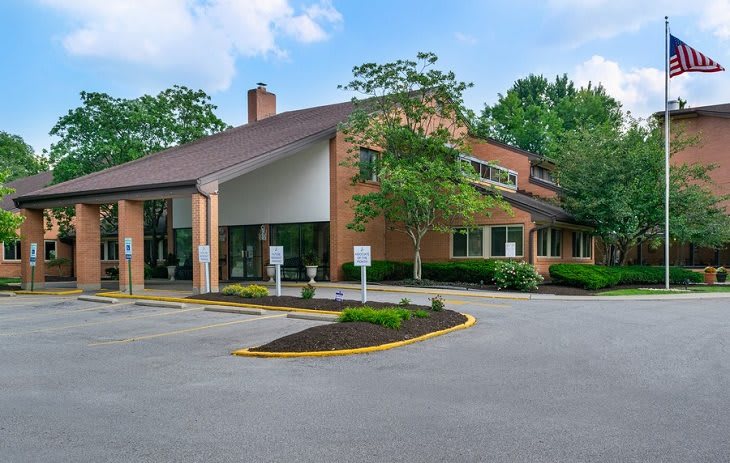 A two-story brick office building surrounded by trees with a well-maintained parking lot.