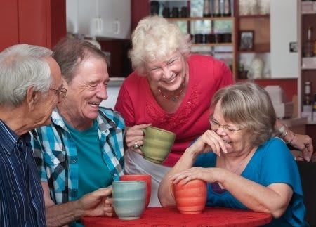 A group of seniors enjoying coffee and laughter together indoors.