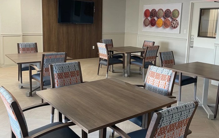 A modern dining area with neatly arranged tables and chairs, featuring wall art and a television.