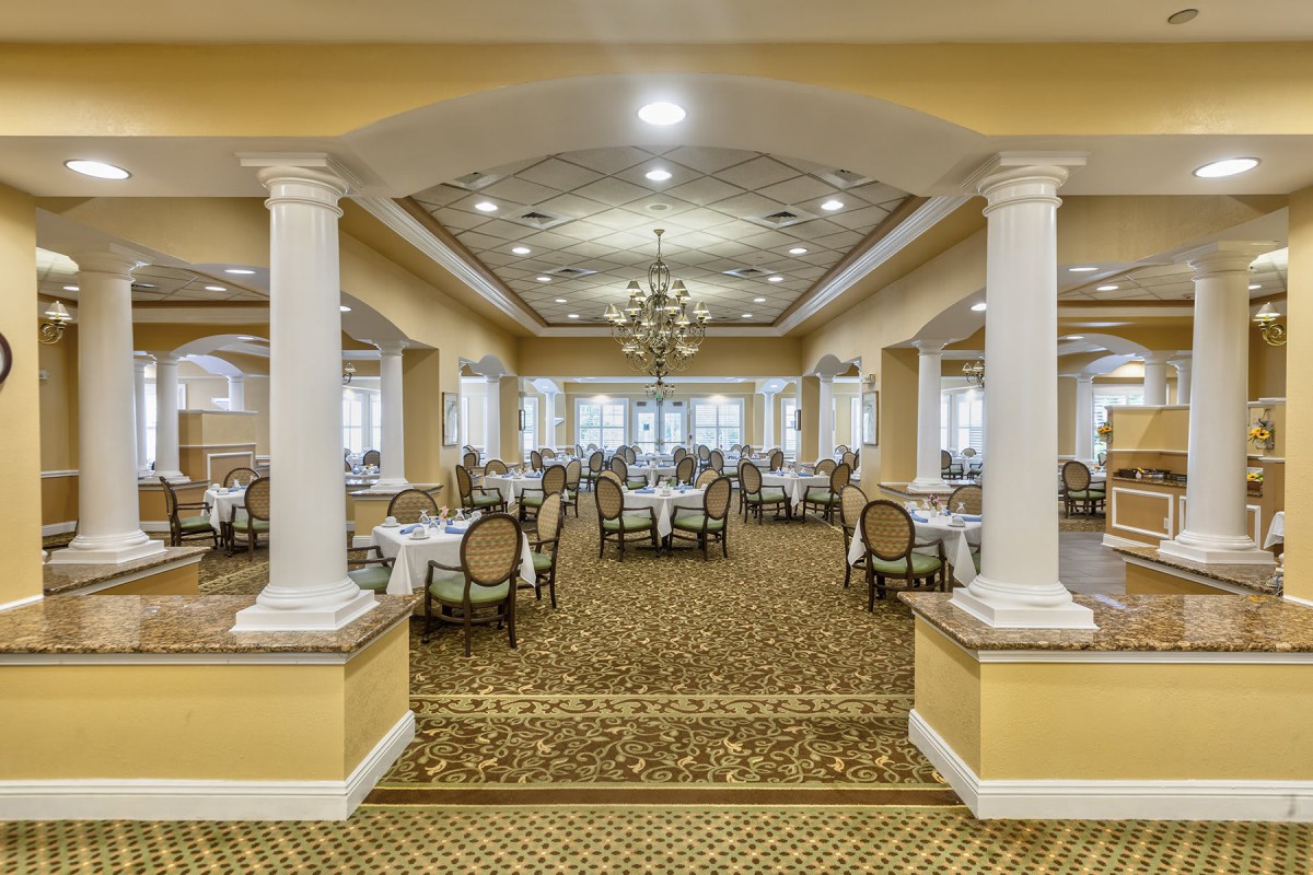 A spacious and elegant dining area featuring chandeliers, pillars, and neatly arranged tables with chairs.
