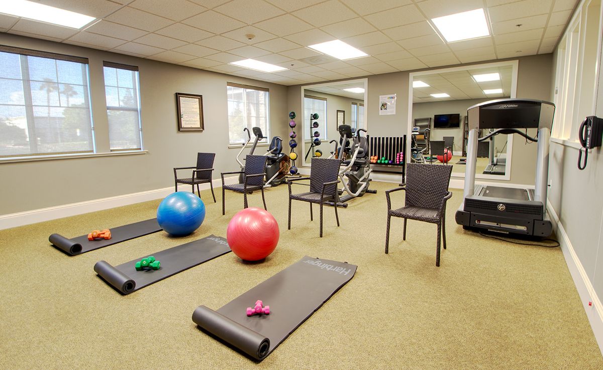 A well-equipped gym featuring yoga mats, fitness balls, exercise machines, and chairs for various workouts.