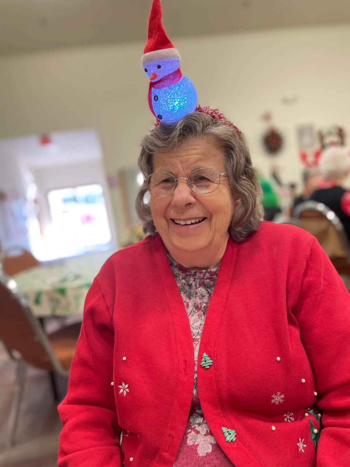 A woman smiling while wearing a festive headband and red sweater indoors.