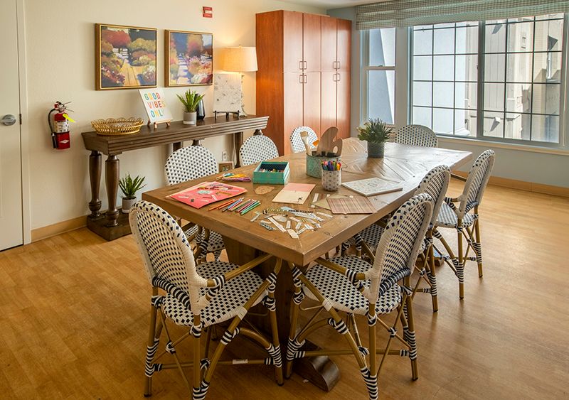 A cozy dining area with a wooden table, surrounded by patterned chairs, artwork on the walls, and lush plants adding a touch of nature.