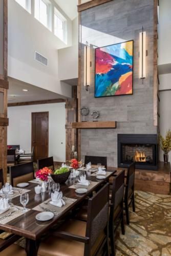 A modern dining room with a well-set table, vibrant artwork, and a cozy fireplace.