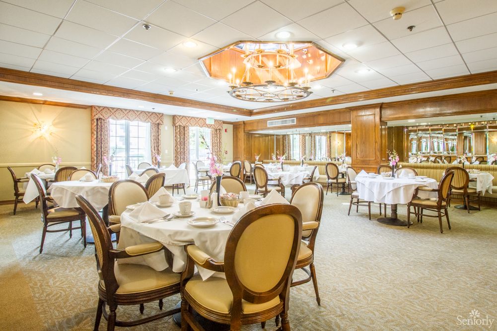 An elegant dining room with formal table settings and a chandelier.