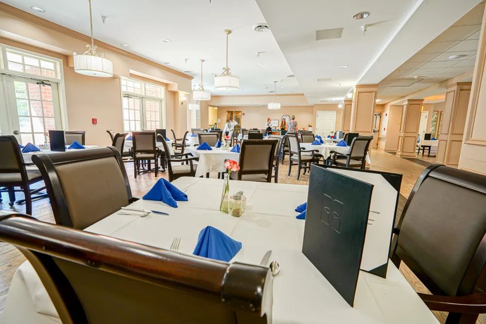 An elegant dining room with tables set for a meal, featuring blue napkins and menus on each table.