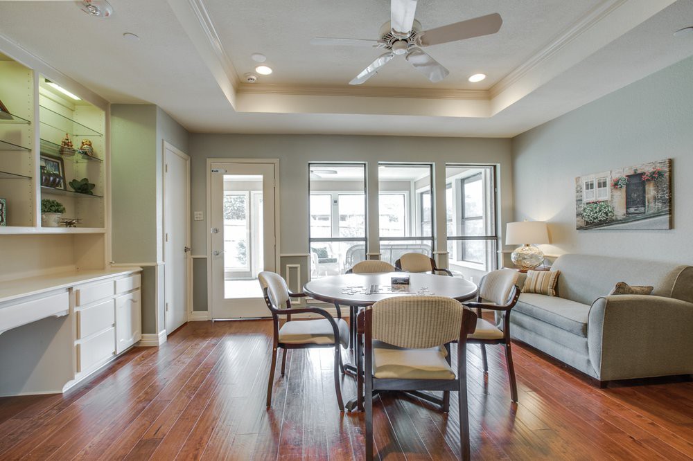 An elegant dining room with a round table, chairs, and a ceiling fan, featuring hardwood floors and large windows.