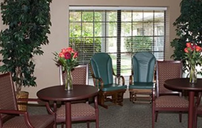 A cozy waiting room with chairs, a table, and a vase of flowers by the window.