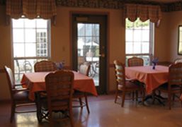 A cozy dining room with tables and chairs, featuring large windows and a door leading outside.