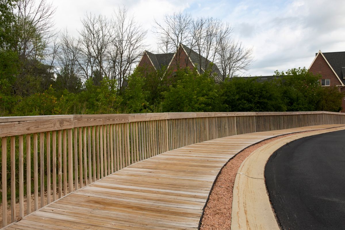 A wooden bridge curves through a natural landscape with trees in the background.