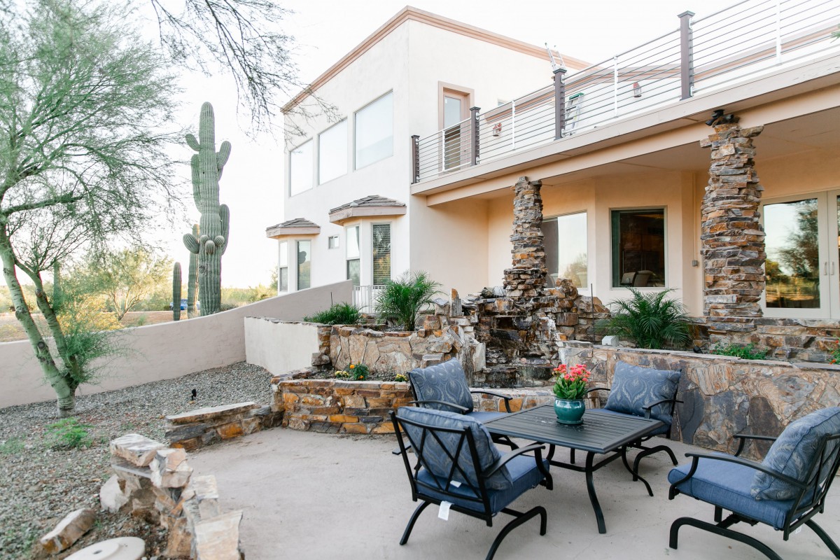 A serene outdoor patio with a stone fountain set in a desert landscape, featuring comfortable patio furniture and distinctive cacti surroundings.