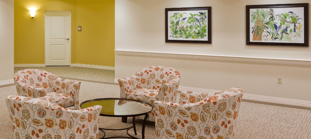 A cozy lobby seating area featuring patterned chairs and a glass coffee table, with framed artwork on the wall.