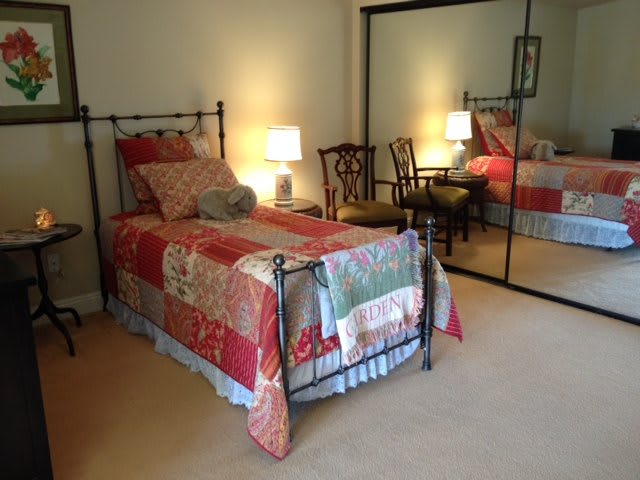 A cozy bedroom with a single bed adorned with a patchwork quilt, reflecting in a mirrored closet door.