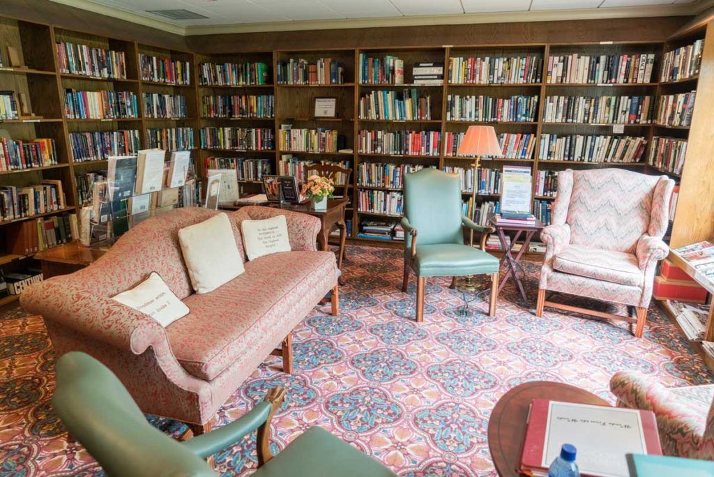 A cozy library room with sofas, armchairs, and bookshelves filled with books.