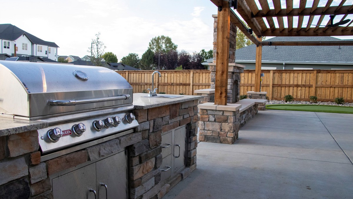 A stylish outdoor kitchen with a barbecue grill and stone countertops under a wooden pergola.