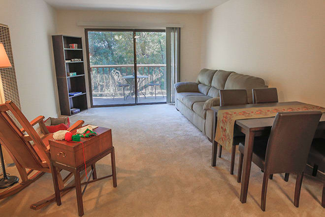 A cozy living room with a sofa, bookshelf, and sliding glass doors leading to a balcony.