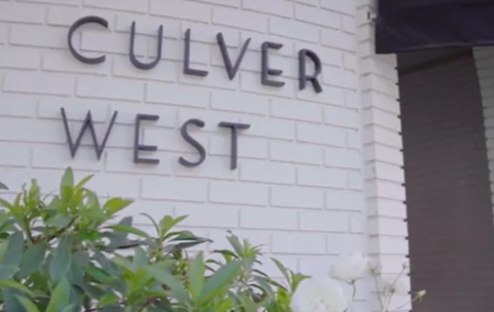A close-up view of a building sign for Culver West with some greenery in the foreground.