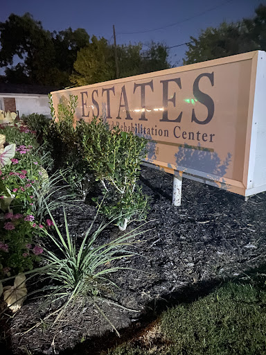 A well-lit sign for an estates rehabilitation center surrounded by plants, captured at night.