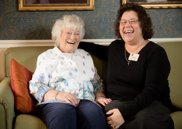 Two women sitting on a couch, smiling and laughing together.