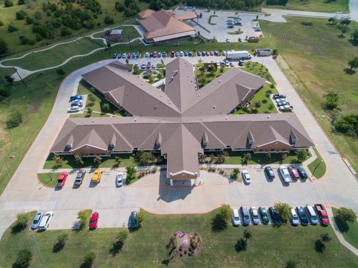 Aerial view of a uniquely designed building surrounded by a parking lot and landscaped greenery.