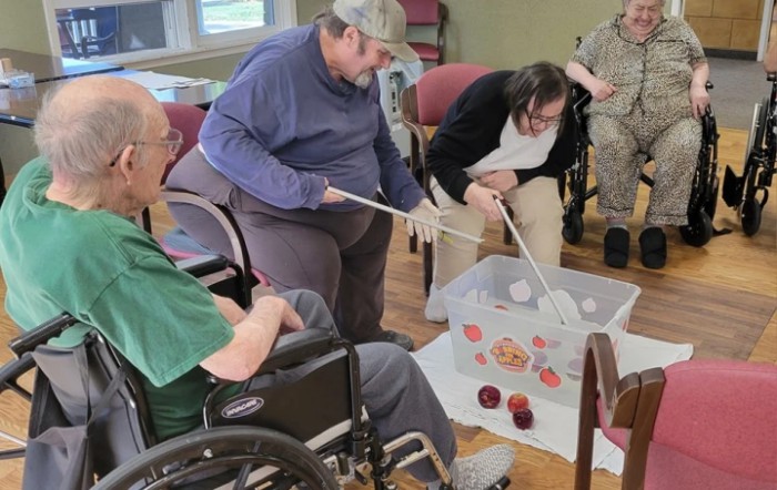 Elderly individuals participating in an engaging group activity involving a white container and various objects.