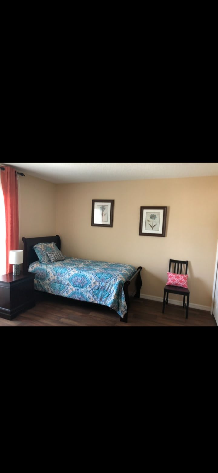 A simple bedroom with a single bed, decorative framed pictures, and a chair beside it.
