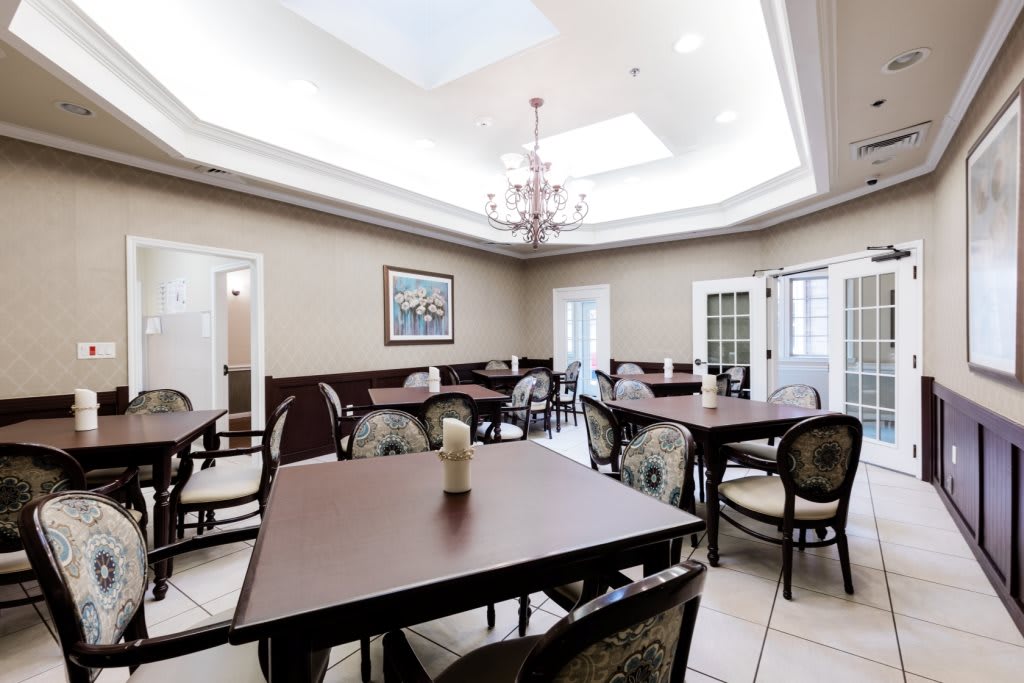 A well-lit dining room featuring multiple tables and chairs, complemented by a chandelier and skylight.