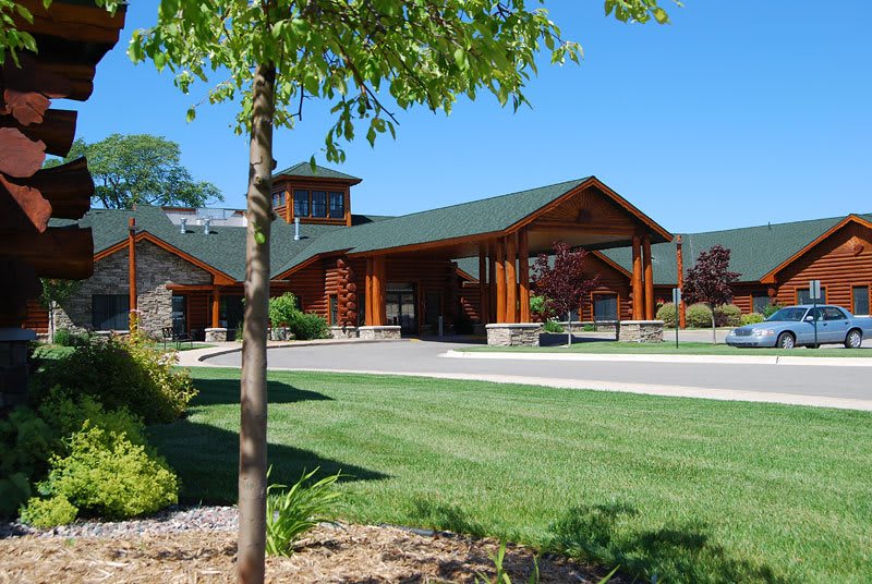 A modern building with a wooden facade set against a clear blue sky, surrounded by well-maintained grass and trees.