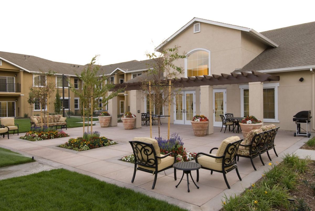 A serene courtyard with patio chairs and a pergola, surrounded by landscaped greenery.