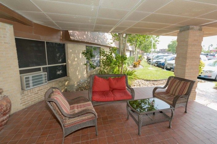 A cozy outdoor seating area with cushioned chairs and a glass-top table under a covered patio.