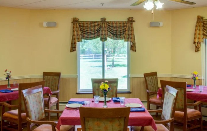 A cozy dining room with tables and chairs neatly arranged by a window with decorative curtains.
