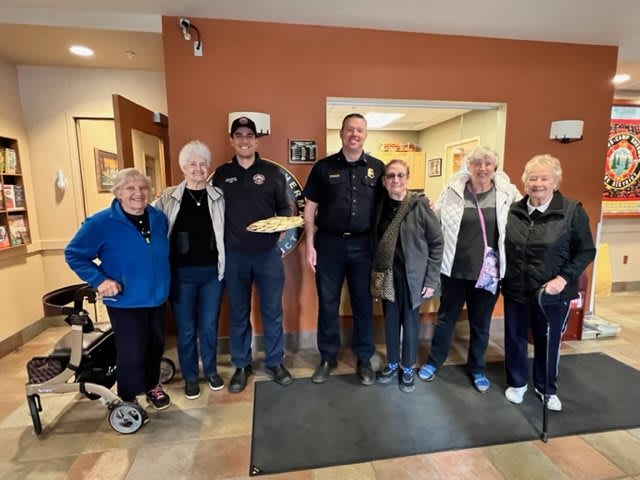 A group of seniors posing with two firefighters indoors.
